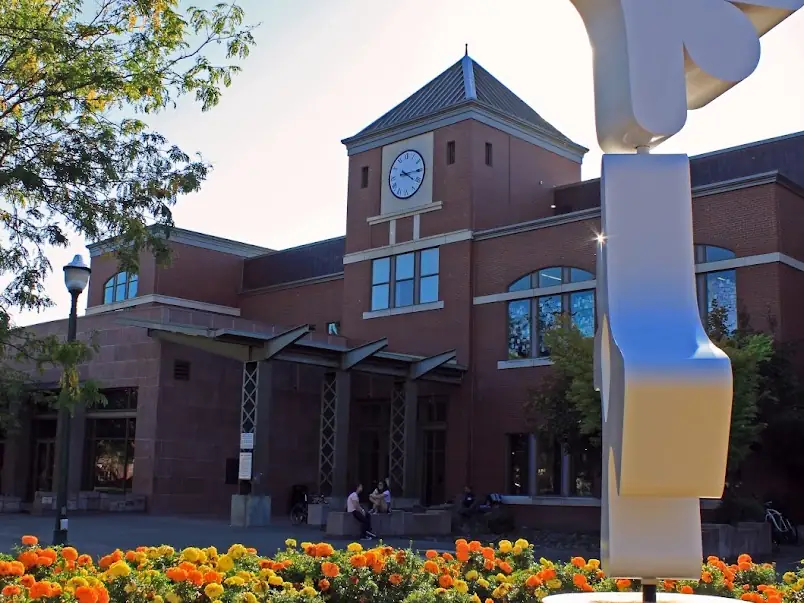 Brick Puyallup Public Library with a clock tower, marigold flower beds and a white abstract sculpture out front