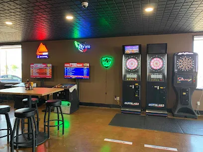 Inside Top Gun Bar and Grill with neon beer signs, two electronic dartboards and stools at a high table